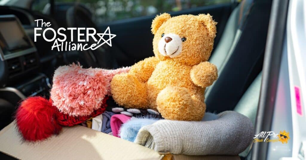 Soft teddy bear sitting among clothing in vehicle trunk for charity donation.