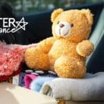 Soft teddy bear sitting among clothing in vehicle trunk for charity donation.