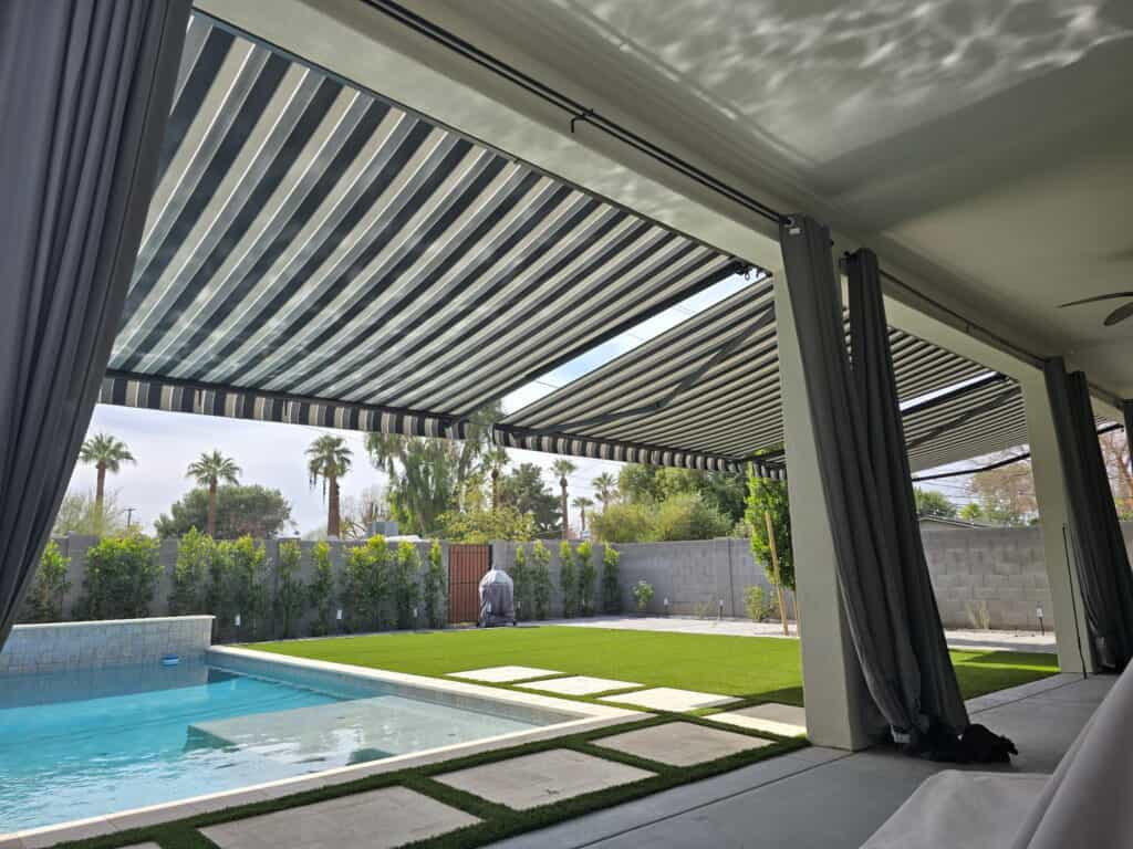 View From Underneath a Modern Striped Retractable Awning Shading a Luxury Poolside Patio and Artificial Turf Backyard